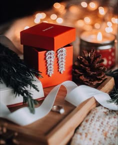 an orange box with two earrings on it next to some pine cones and christmas lights