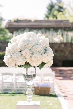 a vase filled with white flowers sitting on top of a table next to an empty chair