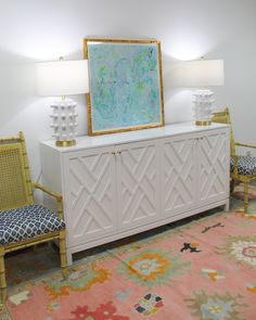 a room with two chairs and a large painting on the wall above it, in front of a colorful area rug