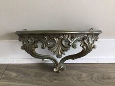 an ornate metal shelf on the floor in front of a white wall and wood floor