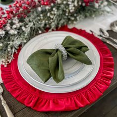 a red and white place setting with green napkins, silverware and greenery