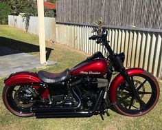 a red and black motorcycle parked on top of a grass covered field next to a fence