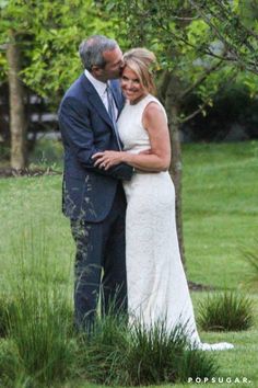 a man and woman standing next to each other in front of a tree with their arms around each other