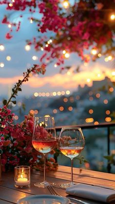 two wine glasses sitting on top of a wooden table next to a vase filled with flowers