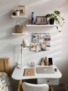 a white desk topped with a laptop computer next to a wall mounted shelf filled with pictures