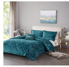 a bed with teal comforter and pillows in a room next to a window