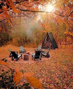 an outdoor fire pit surrounded by chairs and tables in the fall forest with leaves on the ground