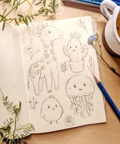 an open notebook with drawings of animals and plants on it next to a cup of coffee