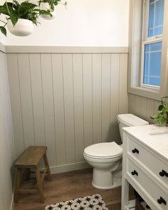 a white toilet sitting in a bathroom next to a sink and wooden floored walls