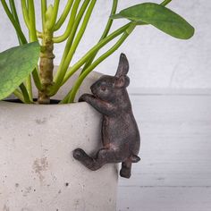 a small rabbit figurine sitting on its hind legs next to a potted plant