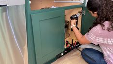 a woman kneeling down in front of a green cabinet with tools on the bottom and inside