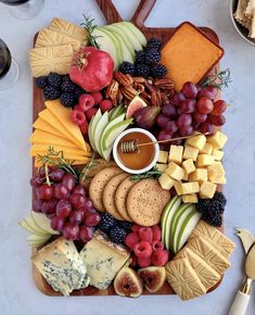 an assortment of cheeses, fruits and crackers on a platter with honey