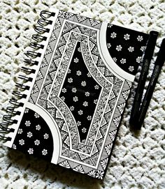 a black and white notebook with an intricate design on it next to a pair of pencils