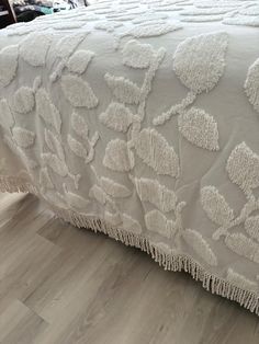 a white bedspread with flowers and fringes on the edge is sitting on a wooden floor