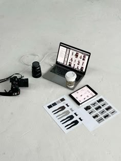 an open laptop computer sitting on top of a white table next to a camera and other items