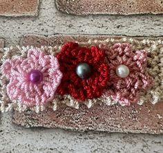 two crocheted flowers with pearls are on a brick wall and one is pink, the other is red