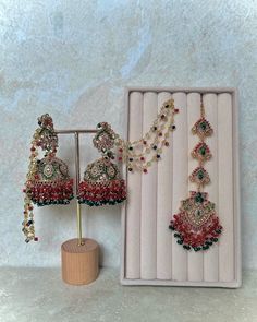 two pairs of red and green beaded earrings next to a wooden stand with jewelry on it