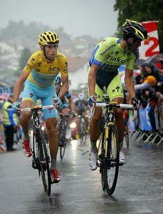 two bicyclists are racing down the road in front of a large crowd