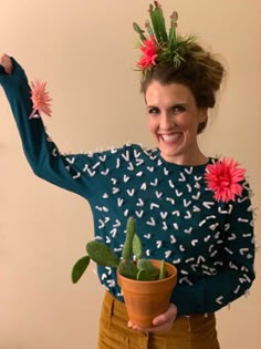 a woman is holding a potted plant with flowers on her head and wearing a sweater