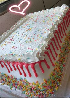 a large white cake with sprinkles on it and a neon sign in the background