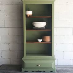 a green china cabinet with bowls on top