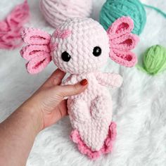 a hand holding a pink crocheted stuffed animal next to two balls of yarn