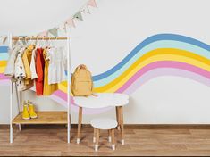 a child's clothing rack in front of a rainbow painted wall