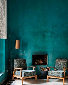 two chairs and a table in front of a blue wall with a fire place on it