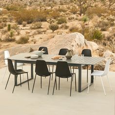 an outdoor table with chairs and plates on it in the middle of desert land, surrounded by large rocks