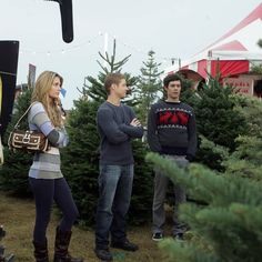 three people standing in front of christmas trees