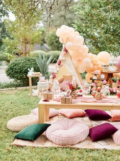 an outdoor party with balloons and pillows on the ground, including a table full of food