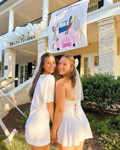 two young women standing in front of a building with a banner on it's roof