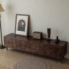 a wooden sideboard sitting on top of a hard wood floor next to a lamp