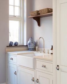 a white kitchen sink sitting under a window next to a wooden shelf with baskets on it