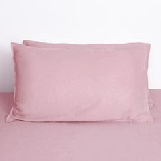 two pink pillows sitting on top of a bed next to a pillow case with the cover pulled down