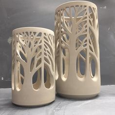 two white vases sitting next to each other on top of a gray tablecloth