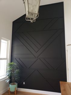 a room with a lamp, potted plant and large black paneled wall in the background