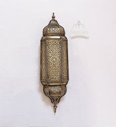 an ornate brass wall light hanging on a white wall