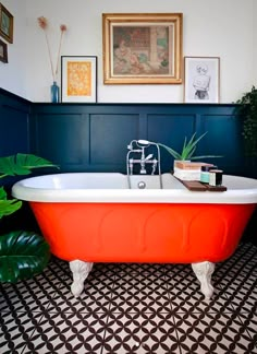 an orange bathtub in a bathroom with black and white flooring, framed pictures on the wall