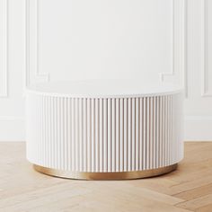 a white and gold round table on a wooden floor in front of a white wall