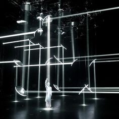 a woman standing in front of an array of spotlights on a black stage with white lights