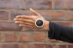 a woman's hand with a coffee cup in front of a brick wall and pointing at the camera