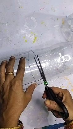 two hands holding scissors over a piece of paper with writing on it and plastic bottle in the background