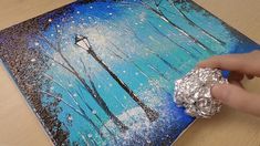 someone is painting on a piece of wood with silver foil and blue paint, while holding a ring in their left hand