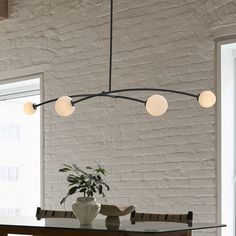 a dining room table with a vase on it and lights hanging from the ceiling above