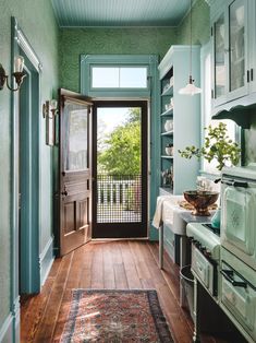 a kitchen with green walls and wooden floors, an open door leading to the outside