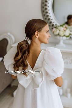 a woman with long hair wearing a white dress standing in front of a mirror and looking into the distance