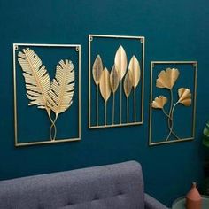 three gold metal wall art pieces on a blue wall next to a gray couch and potted plant