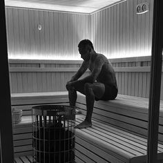 a man sitting on top of a wooden bench next to a trash can in a sauna