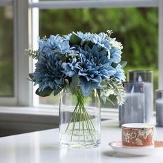 a glass vase with blue flowers on a table next to a cup and saucer